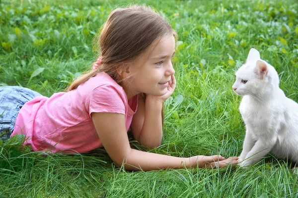 Kleine meisje en witte kat liggen op gras buitenshuis — Stockfoto