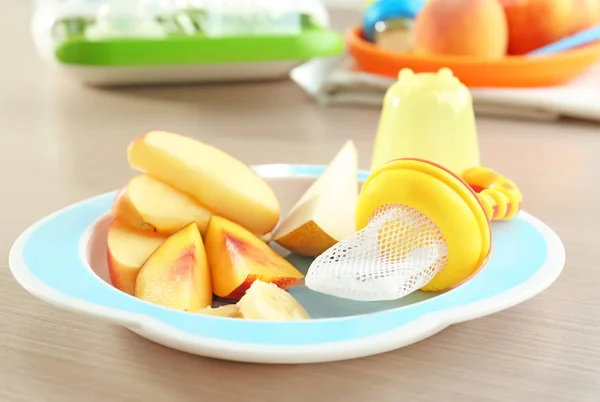 Prato com frutas fatiadas e mordedor de bebê na mesa — Fotografia de Stock