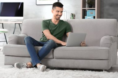 Evde kanepe üzerinde modern dizüstü bilgisayar ile genç adam