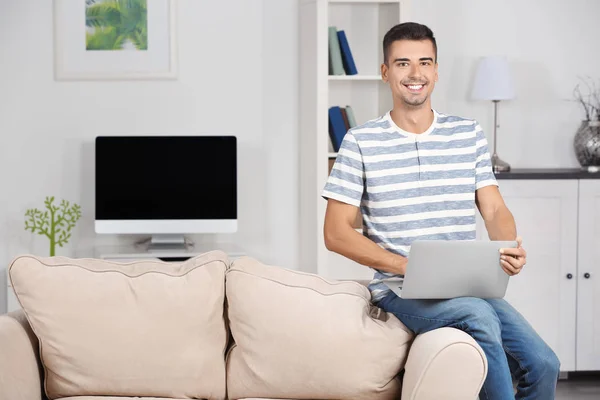 Hombre joven con portátil moderno en el sofá en casa —  Fotos de Stock