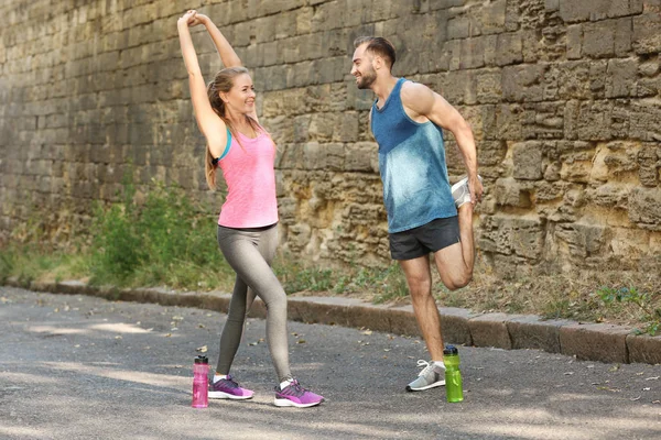 Joven hombre y mujer en ropa deportiva calentamiento al aire libre — Foto de Stock