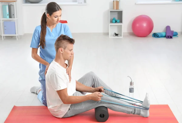 Fisioterapeuta que trabaja con un paciente masculino joven en la clínica — Foto de Stock