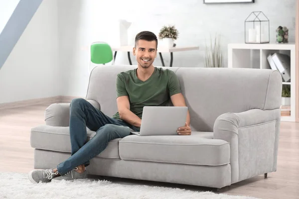 Молодий чоловік з сучасним ноутбуком на дивані вдома — стокове фото