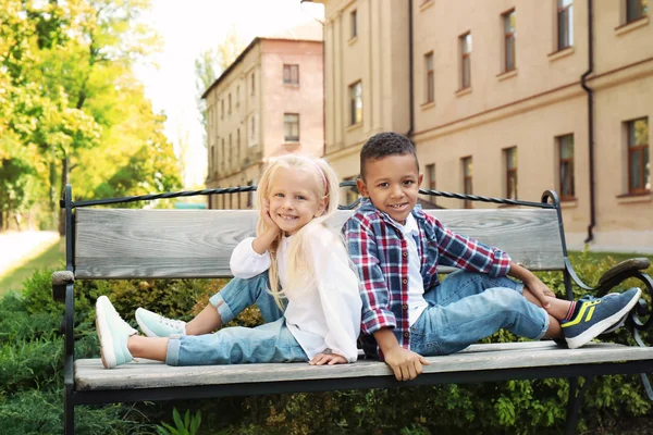 Bonito crianças na moda sentadas no banco ao ar livre — Fotografia de Stock