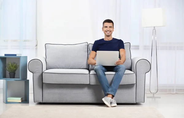 Молодий чоловік з сучасним ноутбуком на дивані вдома — стокове фото