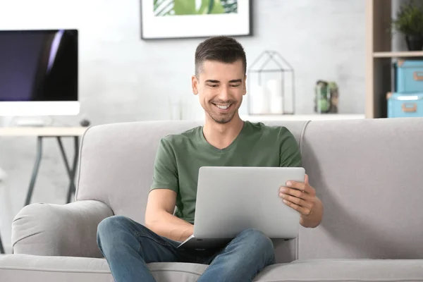 Giovane con laptop moderno sul divano di casa — Foto Stock
