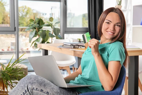 Ung kvinna använder laptop medan du håller kreditkort hemma. Internet shopping koncept — Stockfoto