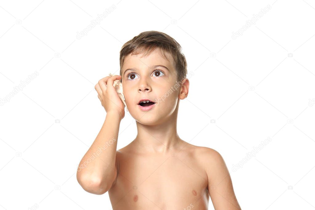 Cute little boy listening sound of sea in shell on white background