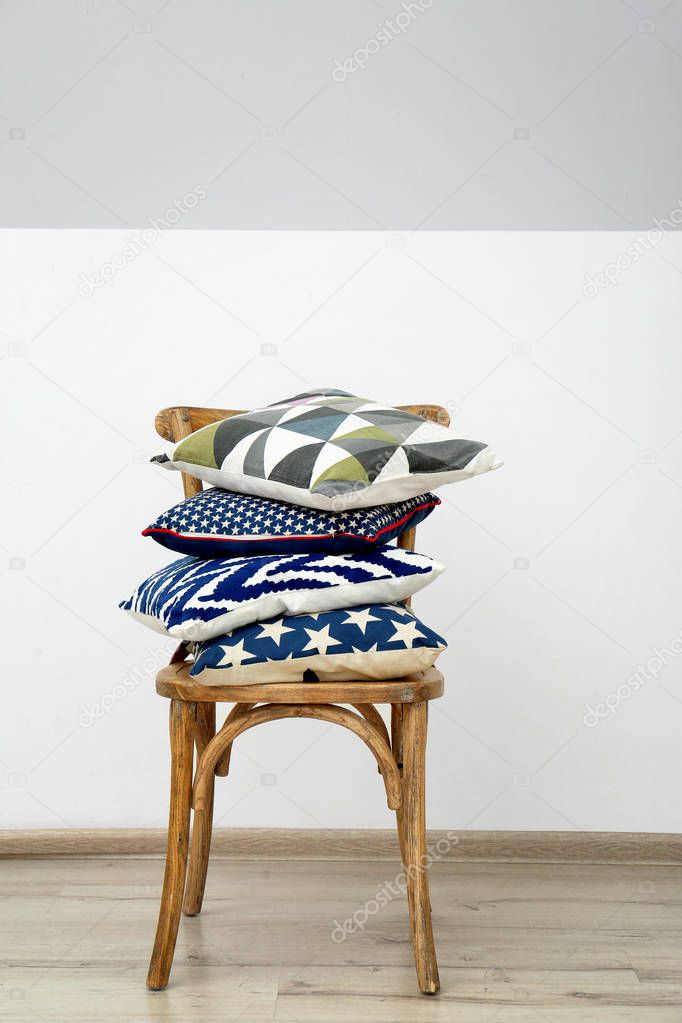 Wooden chair with colorful pillows near light wall
