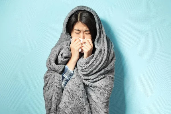 Mujer joven enferma envuelta en manta sobre fondo de color —  Fotos de Stock