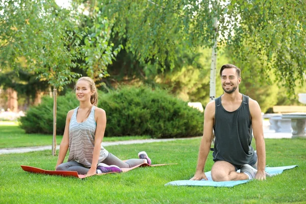 Joven hombre y mujer haciendo ejercicios sobre esteras de yoga en el parque — Foto de Stock