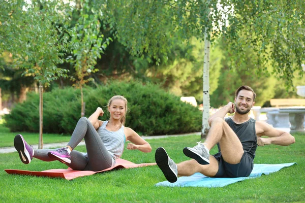 Joven hombre y mujer haciendo ejercicios sobre esteras de yoga en el parque — Foto de Stock