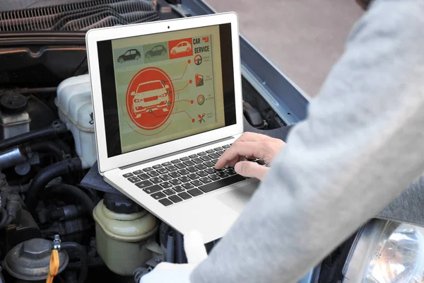 Mecánico masculino joven usando el diagnóstico de la computadora mientras que repara coche —  Fotos de Stock