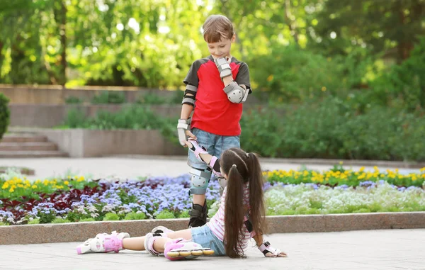 Leuke jongen op rolschaatsen helpen meisje in park opstaan — Stockfoto