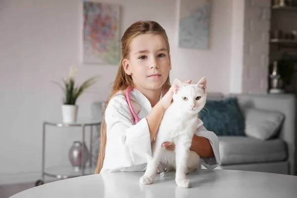 Menina em casaco médico e gato branco na mesa dentro de casa — Fotografia de Stock