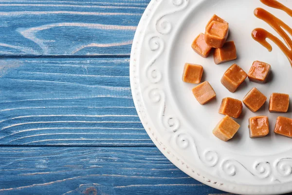 Plate with tasty caramel candies on wooden background — Stock Photo, Image