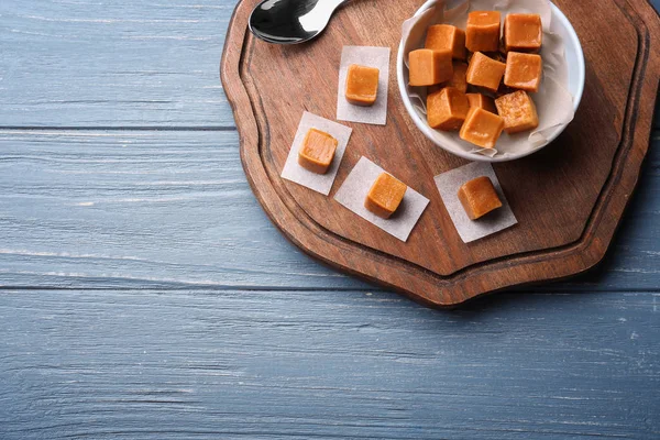 Board with tasty caramel candies on wooden background — Stock Photo, Image