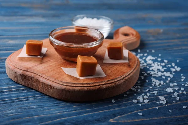 Papan dengan permen karamel lezat dan saus di latar belakang kayu — Stok Foto