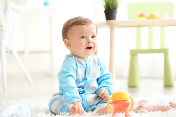 Cute baby with bottle of water sitting on carpet at home — Stock Photo, Image