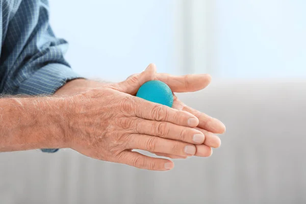 Руки пожилого человека, делающего упражнения с резиновым мячом на размытом фоне — стоковое фото