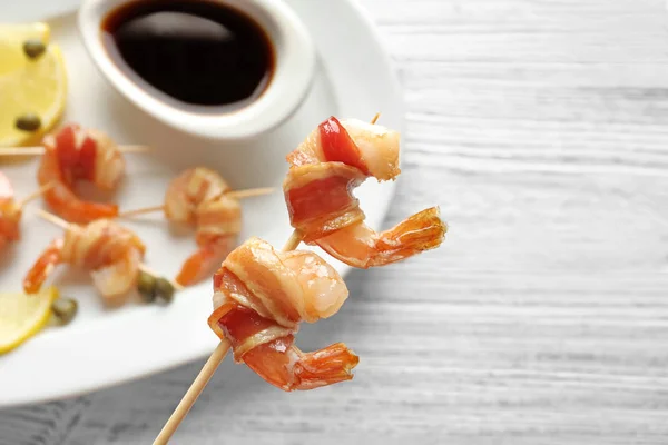 Bacon-wrapped shrimps on skewer over plate — Stock Photo, Image