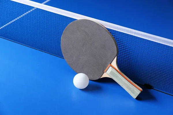 Raqueta de ping pong y pelota cerca de la red en la mesa — Foto de Stock