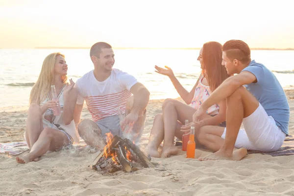 Grupo de jóvenes atractivos sentados cerca de la hoguera en la playa —  Fotos de Stock