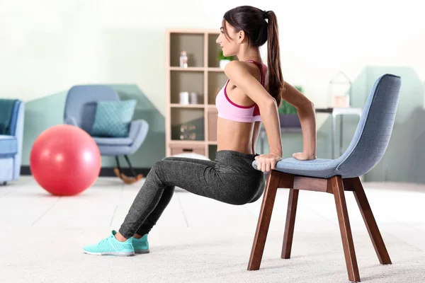 Mulher bonita fazendo exercícios com cadeira em casa — Fotografia de Stock