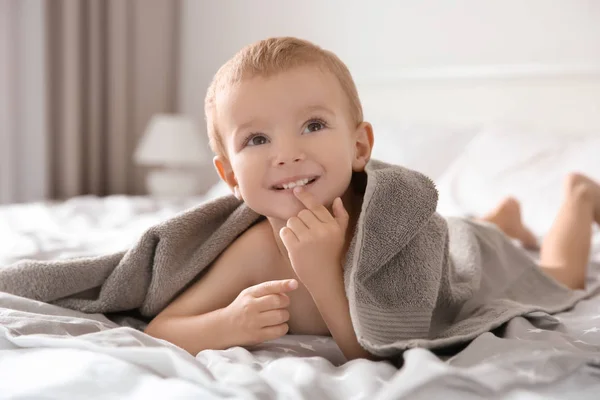 Schattige kleine jongen met handdoek op bed thuis — Stockfoto