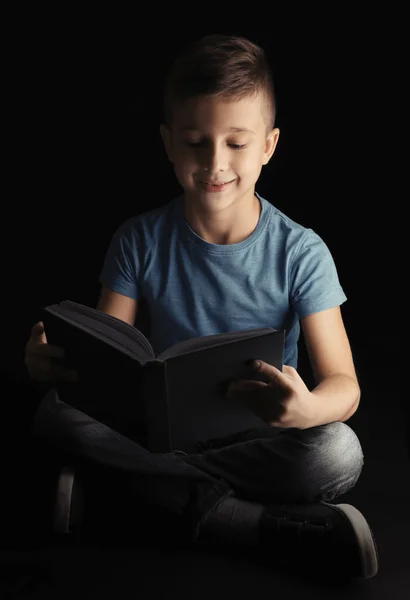 Netter kleiner Junge liest Buch auf dunklem Hintergrund — Stockfoto