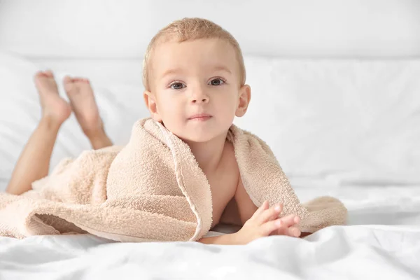 Χαριτωμένο μικρό αγόρι με πετσέτα στο κρεβάτι στο σπίτι — Φωτογραφία Αρχείου