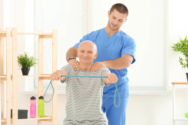 Обучение пожилых пациентов с резинкой под наблюдением врача в физиотерапевтическом центре — стоковое фото
