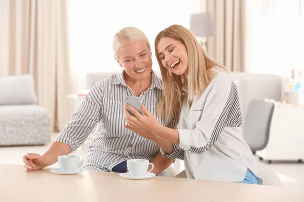 Mujer joven usando el teléfono mientras bebe té con la madre anciana en casa — Foto de Stock