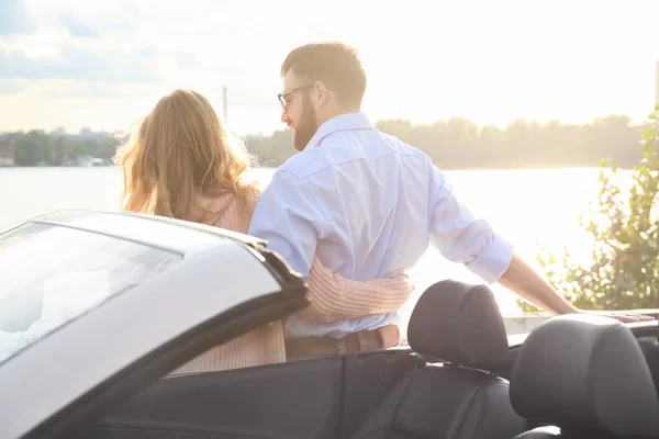 Feliz jovem casal de pé perto de carro na margem do rio — Fotografia de Stock