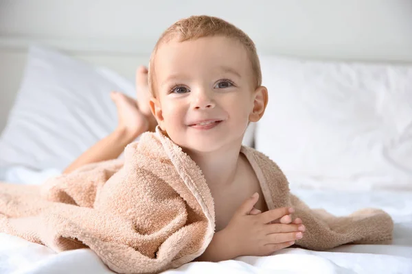 Χαριτωμένο μικρό αγόρι με πετσέτα στο κρεβάτι στο σπίτι — Φωτογραφία Αρχείου