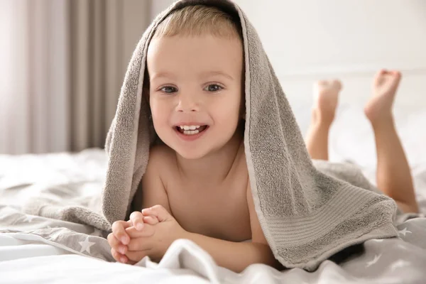 Schattige kleine jongen met handdoek op bed thuis — Stockfoto