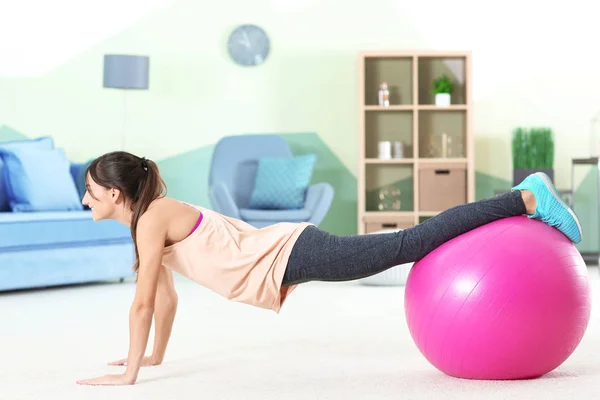 Vacker ung kvinna som gör övningar med fitness boll hemma — Stockfoto