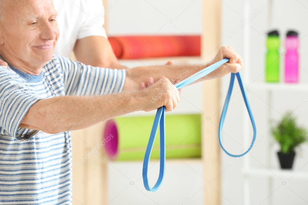 Elderly patient training with rubber band under doctor's supervision in physiotherapy center