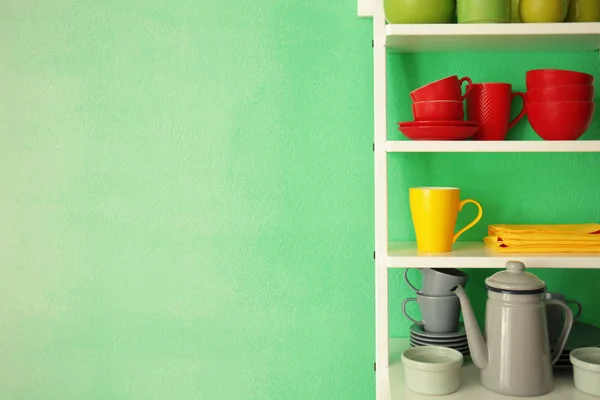 Witte rekken eenheid met keramische servies in de buurt van kleur muur — Stockfoto