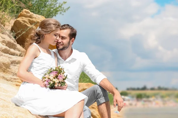 Pareja recién casada sentada en la playa rocosa —  Fotos de Stock