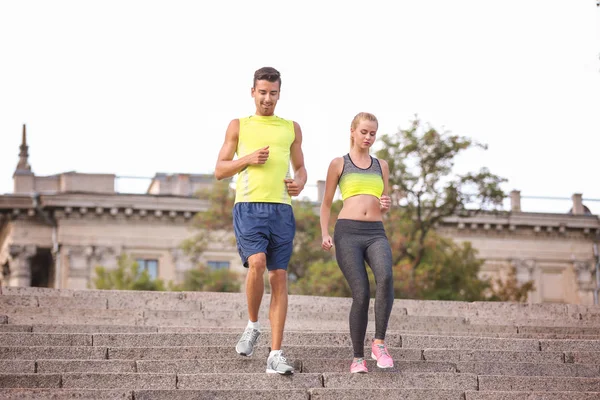 Pareja joven en ropa deportiva caminando escaleras de piedra en la ciudad — Foto de Stock