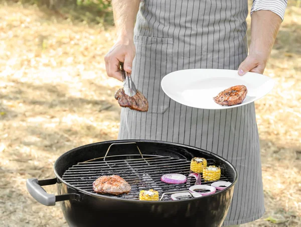 Uomo che cucina gustose bistecche sul barbecue — Foto Stock