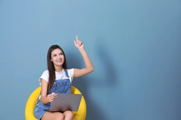 Jonge vrouw met laptop in fauteuil tegen een achtergrond met kleur — Stockfoto