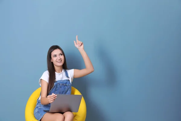 Jeune femme avec ordinateur portable dans le fauteuil sur fond de couleur — Photo