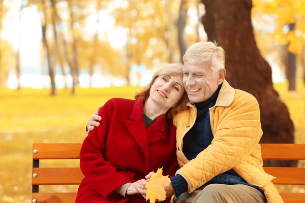 Elderly couple sitting on bench in autumn park — Stock Photo, Image