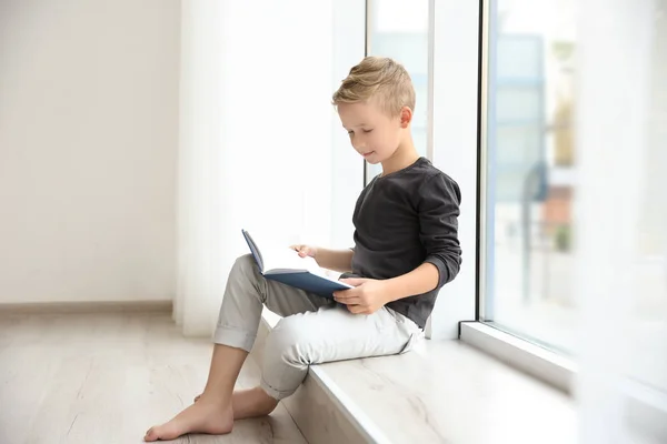 Ładny mały chłopiec czytanie w pobliżu okna w domu — Zdjęcie stockowe
