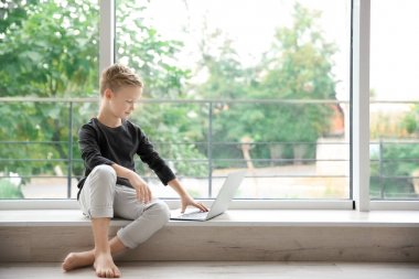 Evde dizüstü bilgisayarı olan şirin bir çocuk.