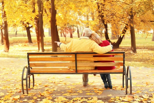 Elderly couple sitting on bench in autumn park — Stock Photo, Image