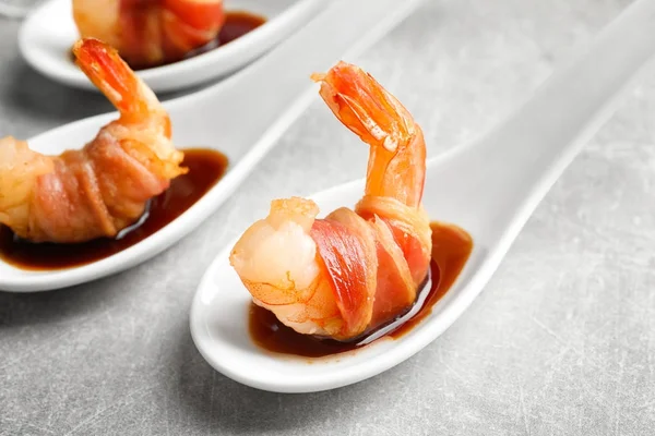 Spoon with shrimp wrapped in bacon and sauce on table — Stock Photo, Image