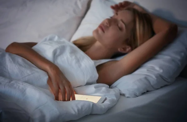 Krásná mladá žena s mobilním telefonem, spí v posteli — Stock fotografie